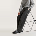 Man leaning on a clear chair in black washed wide-leg panel pants with knee seam and metal rivet detail