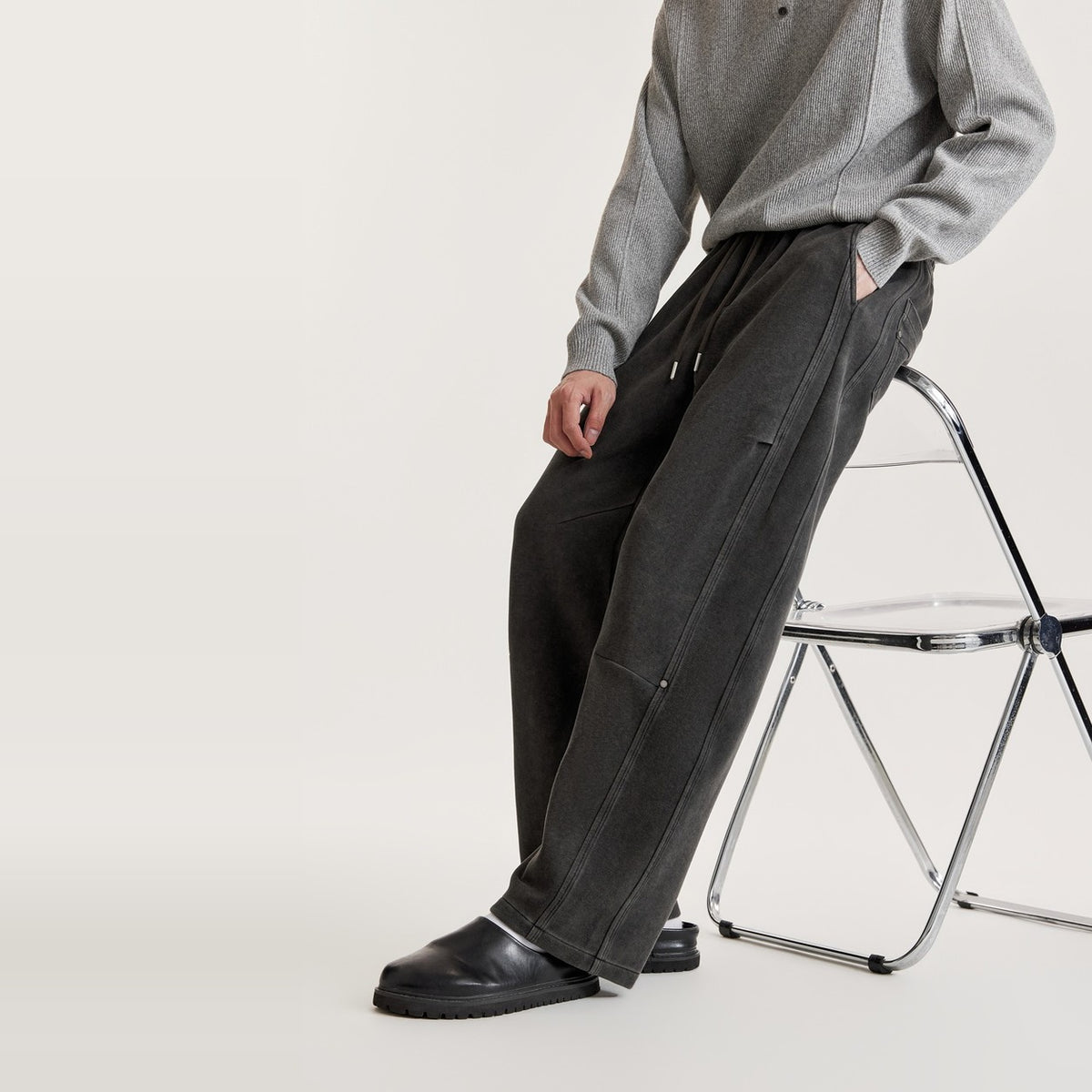 Homme assis portant un pantalon large délavé noir à empiècements, couture au genou et rivets métalliques