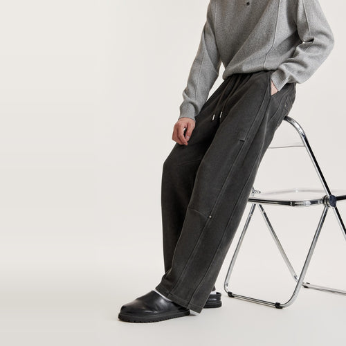 Man leaning on a clear chair in black washed wide-leg panel pants with knee seam and metal rivet detail
