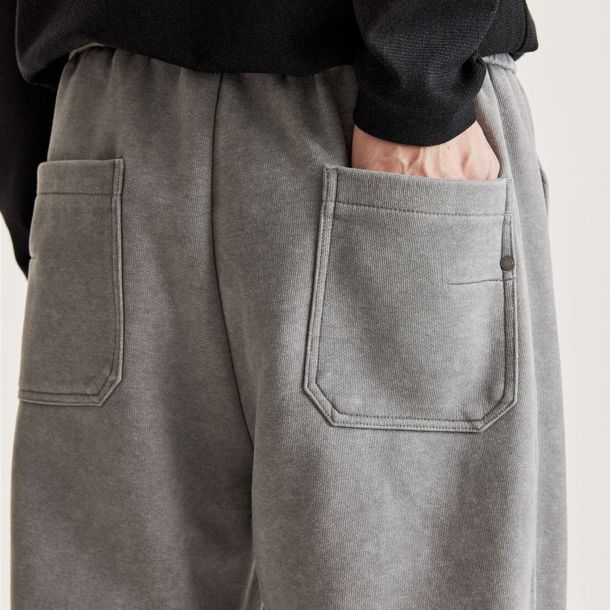 Back view of men's grey washed wide-leg pants with two patch back pockets and metal rivet detail