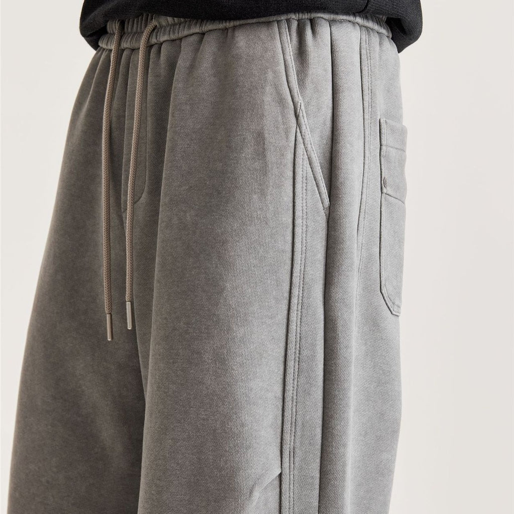 Close-up of men's grey wide-leg pants showing drawstring, angled side pocket and panel seam stitching