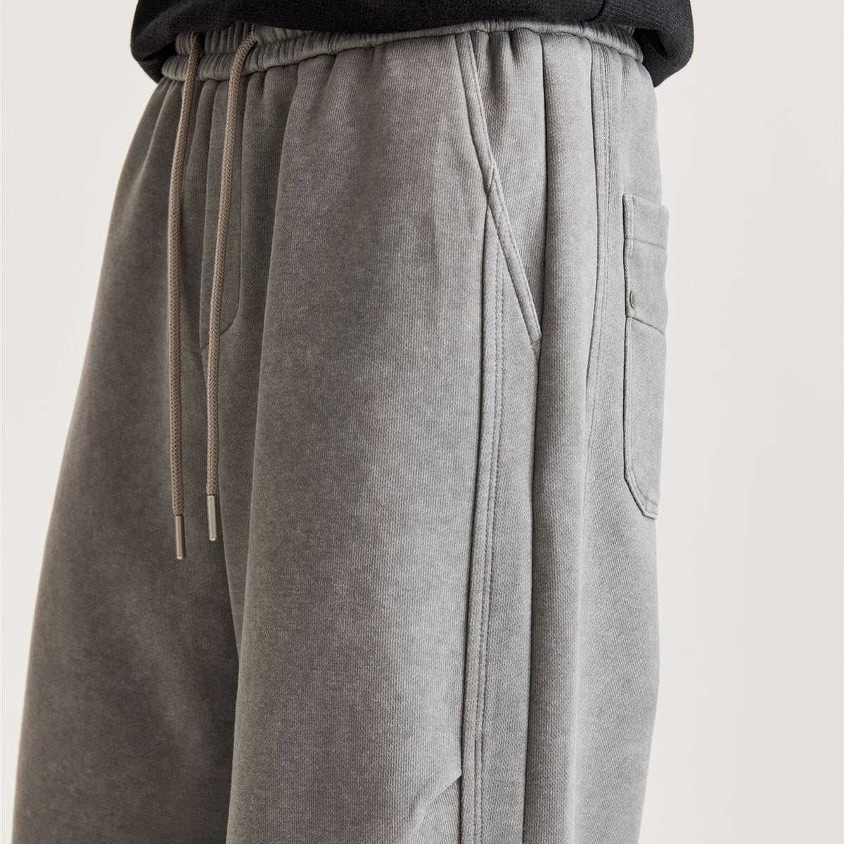 Close-up of men's grey wide-leg pants showing drawstring, angled side pocket and panel seam stitching