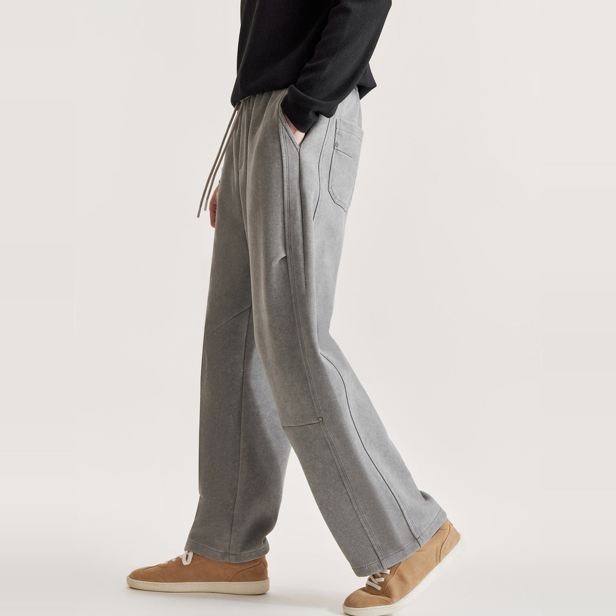 Full-length side view of man walking in grey washed wide-leg panel pants with tan suede sneakers